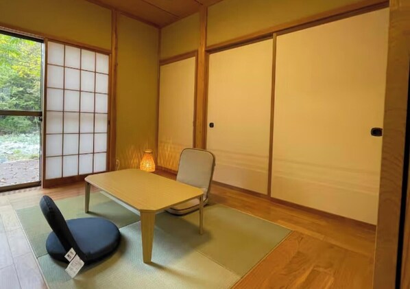 Une pièce de style japonais traditionnel, avec un sol recouvert de tatamis, une table basse, une chaise et des portes coulissantes.