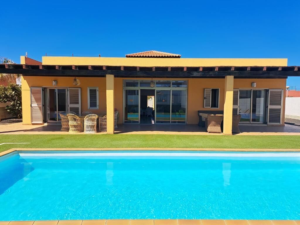 A modern house with a swimming pool, large windows, and a patio with outdoor furniture.