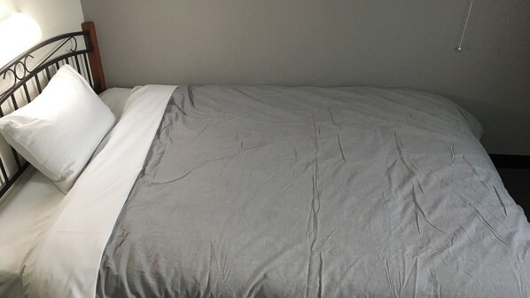 A bed with a gray blanket and white pillows, a wooden headboard, and a wall-mounted light fixture.