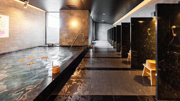 A modern spa with a long hot tub, wooden benches, and a tiled floor. - SUPER HOTEL Kirishima Natural Hot Spring (Kirishima)
