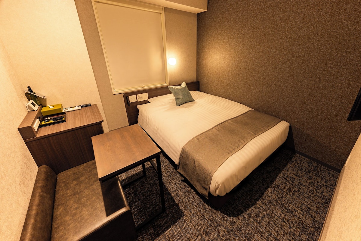 Una habitación de hotel con una cama, un escritorio, una silla, una ventana y piso alfombrado.