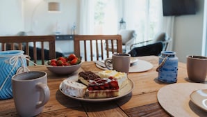 Ruokapöytä, jonka päällä on lautanen täynnä jälkiruokia, kahvimuki ja kulho mansikoita.
