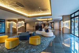 A modern lobby with a reception desk, seating area, and large windows.