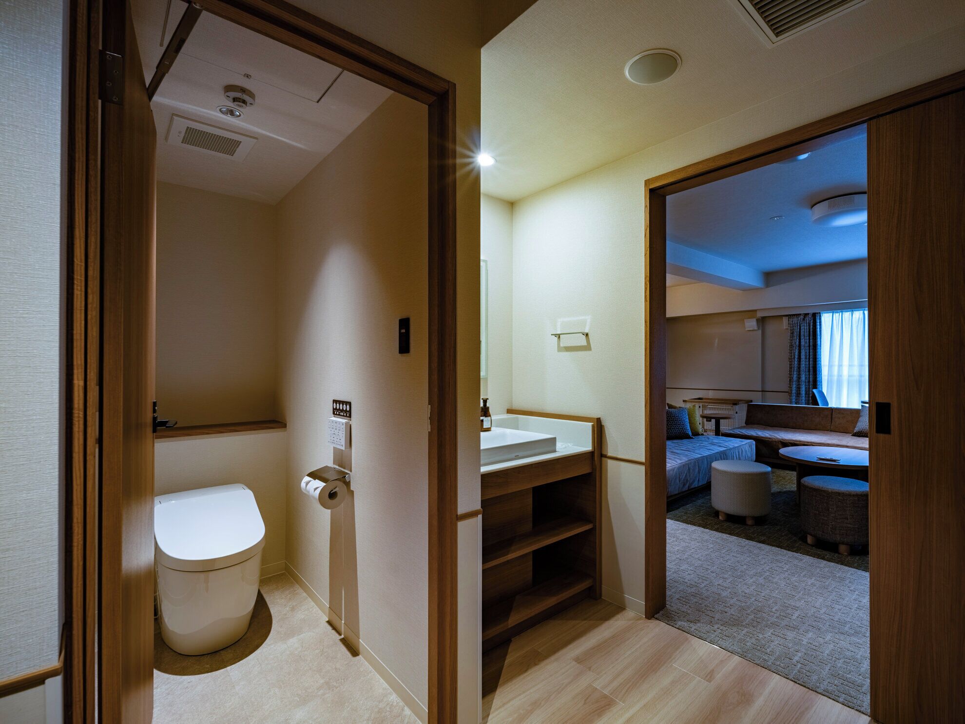 Habitación de hotel pequeña con inodoro, lavamanos y un rincón de descanso con sofá y una mesa redonda.