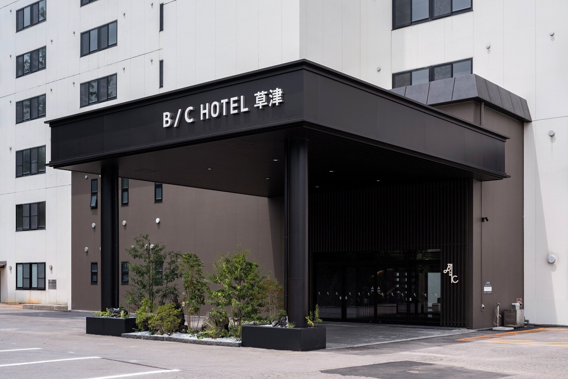 A B/C Hotel entrance with a modern design, featuring a covered entrance area and a parking lot.