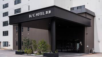 A B/C Hotel entrance with a modern design, featuring a covered entrance area and a parking lot.