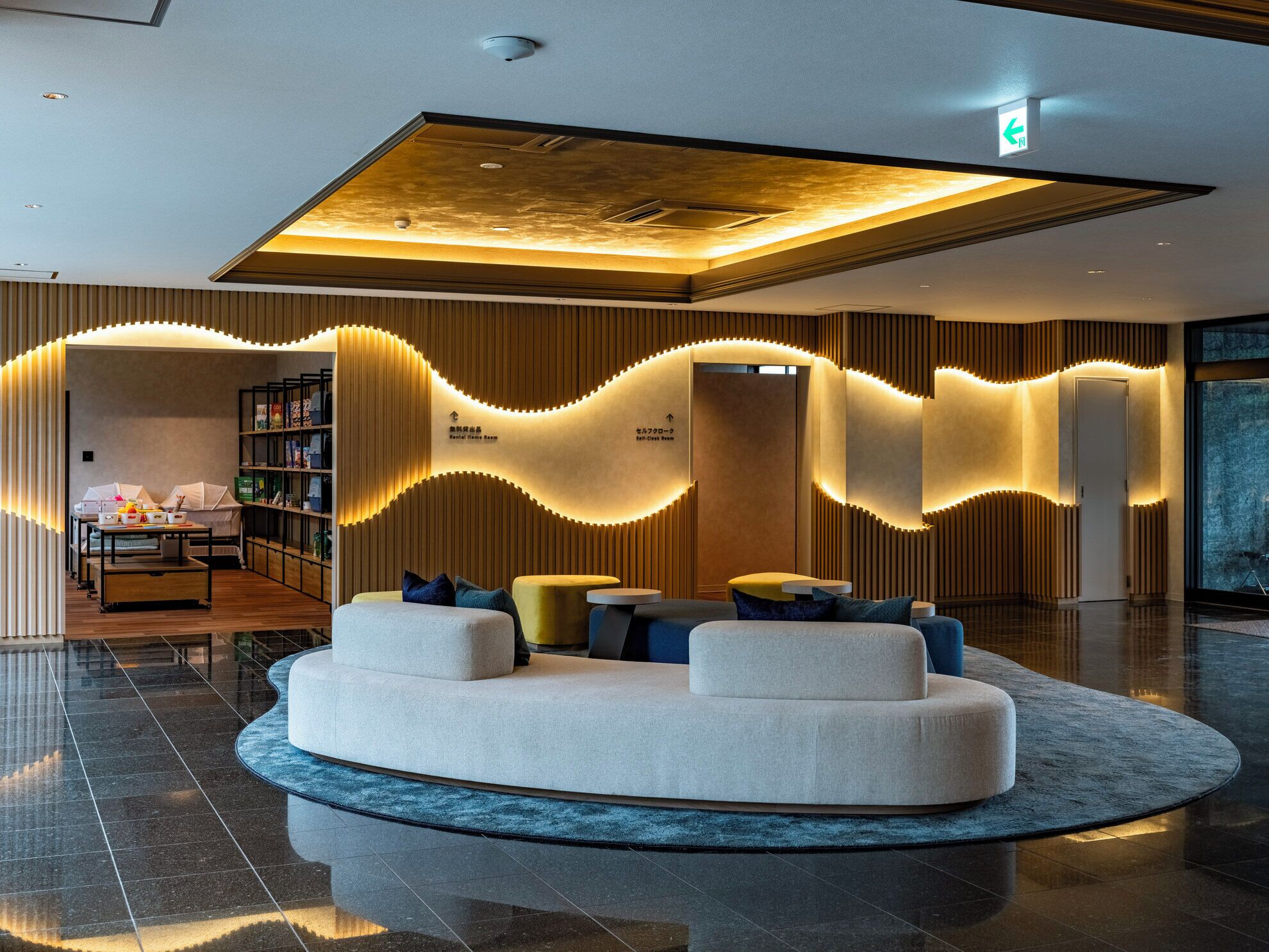 A modern lobby with a central seating area, a reception desk, and a bookshelf.