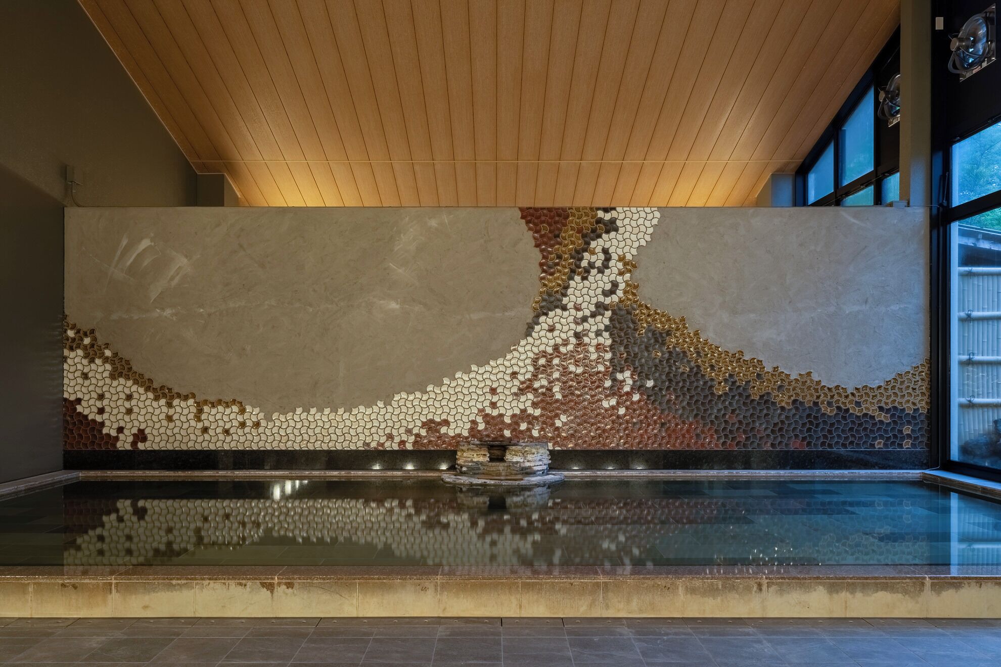 A modern interior with a reflective water feature, a wooden ceiling, and large windows.