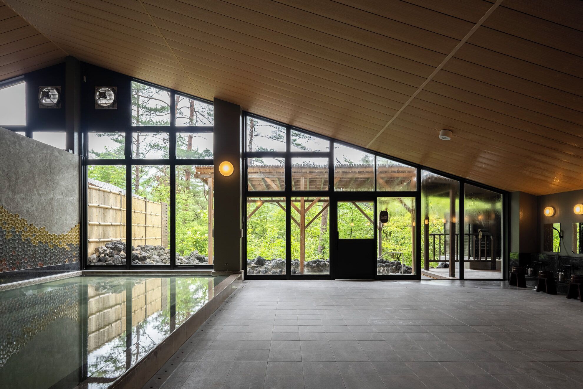 A spacious indoor area with large windows, a pool, and a wooden ceiling.