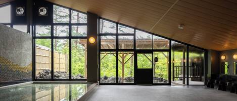 Un espacio interior amplio con ventanas grandes, una piscina y techo de madera.