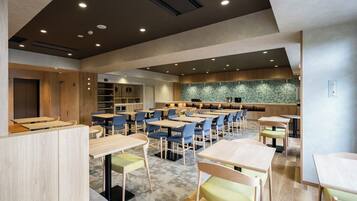 A modern dining area with multiple tables and chairs, a kitchen in the background, and a patterned wall.