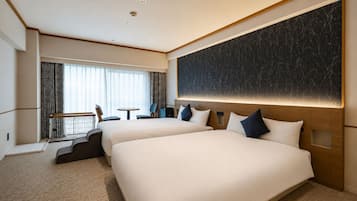 A hotel room with two beds, a desk, and a view of the city.