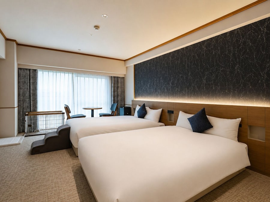 A hotel room with two beds, a desk, and a view of the city.