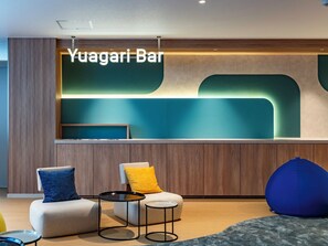 A modern bar area with a sign reading 'Yuagari Bar,' a seating area with a sofa and chairs, and a round table.