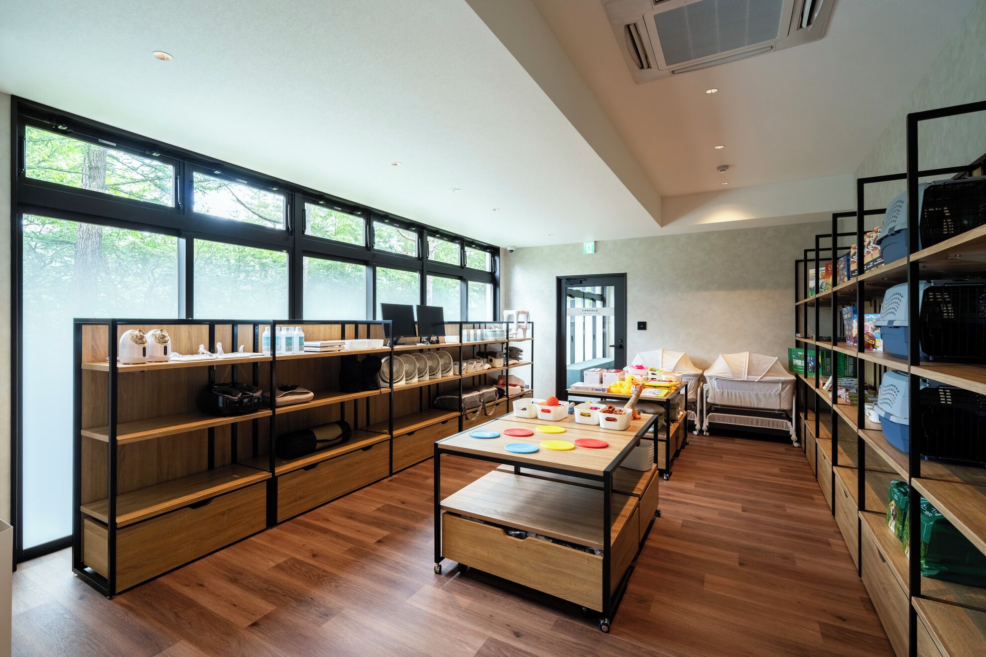 A modern, well-lit room with wooden flooring, large windows, and built-in shelving with various items.
