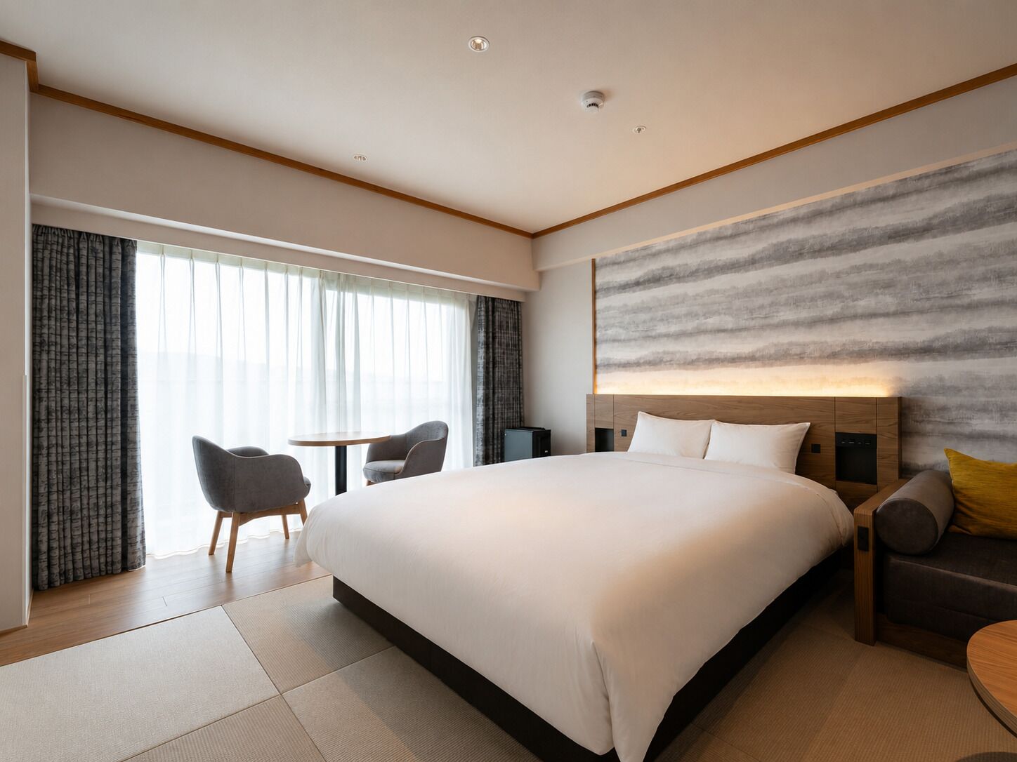 A modern hotel room with a large bed, a desk, and a sofa.