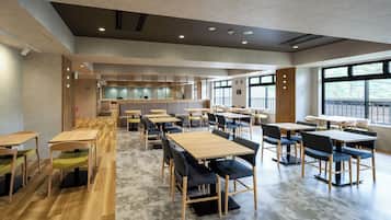 A spacious indoor area with multiple seating arrangements, including tables and chairs, and a kitchen area in the background.