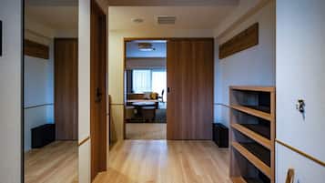 A hallway with wooden flooring, a sliding door leading to a living area with a sofa, coffee table, and a person walking.