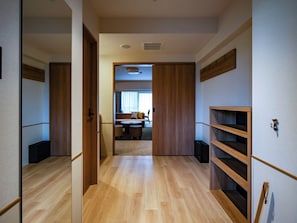 A hallway with wooden flooring, a sliding door leading to a living area with a sofa, coffee table, and a person walking.