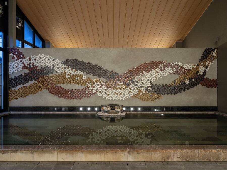 A modern interior with a reflective water feature, wooden ceiling, and a wall with a mosaic pattern.