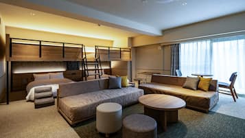 A modern hotel room with a bunk bed, a sofa, a round coffee table, ottomans, and a view of the outdoors.