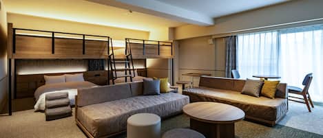A modern hotel room with a bunk bed, a sofa, a round coffee table, ottomans, and a view of the outdoors.