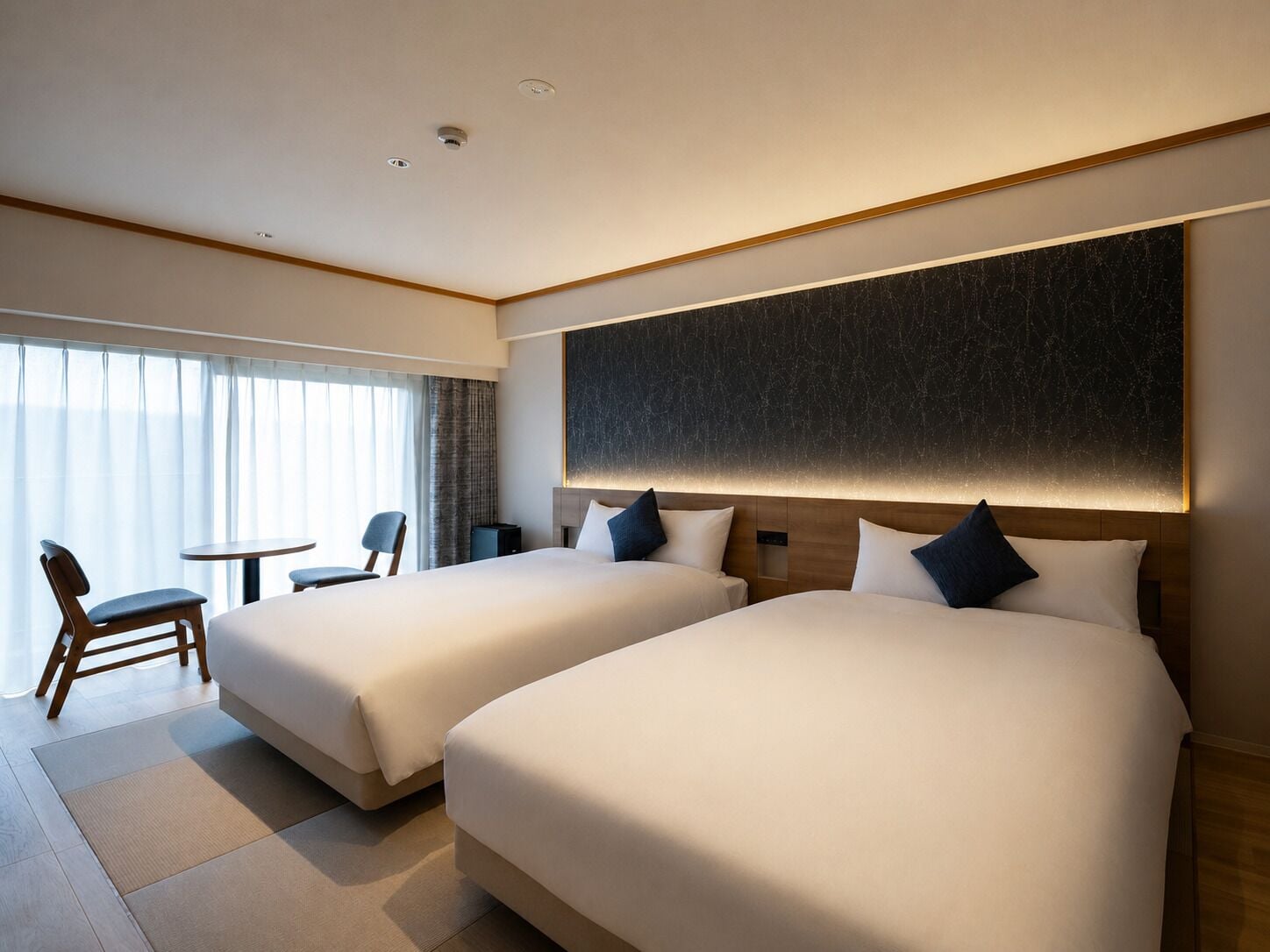 A hotel room with two beds, a desk, and a chair.