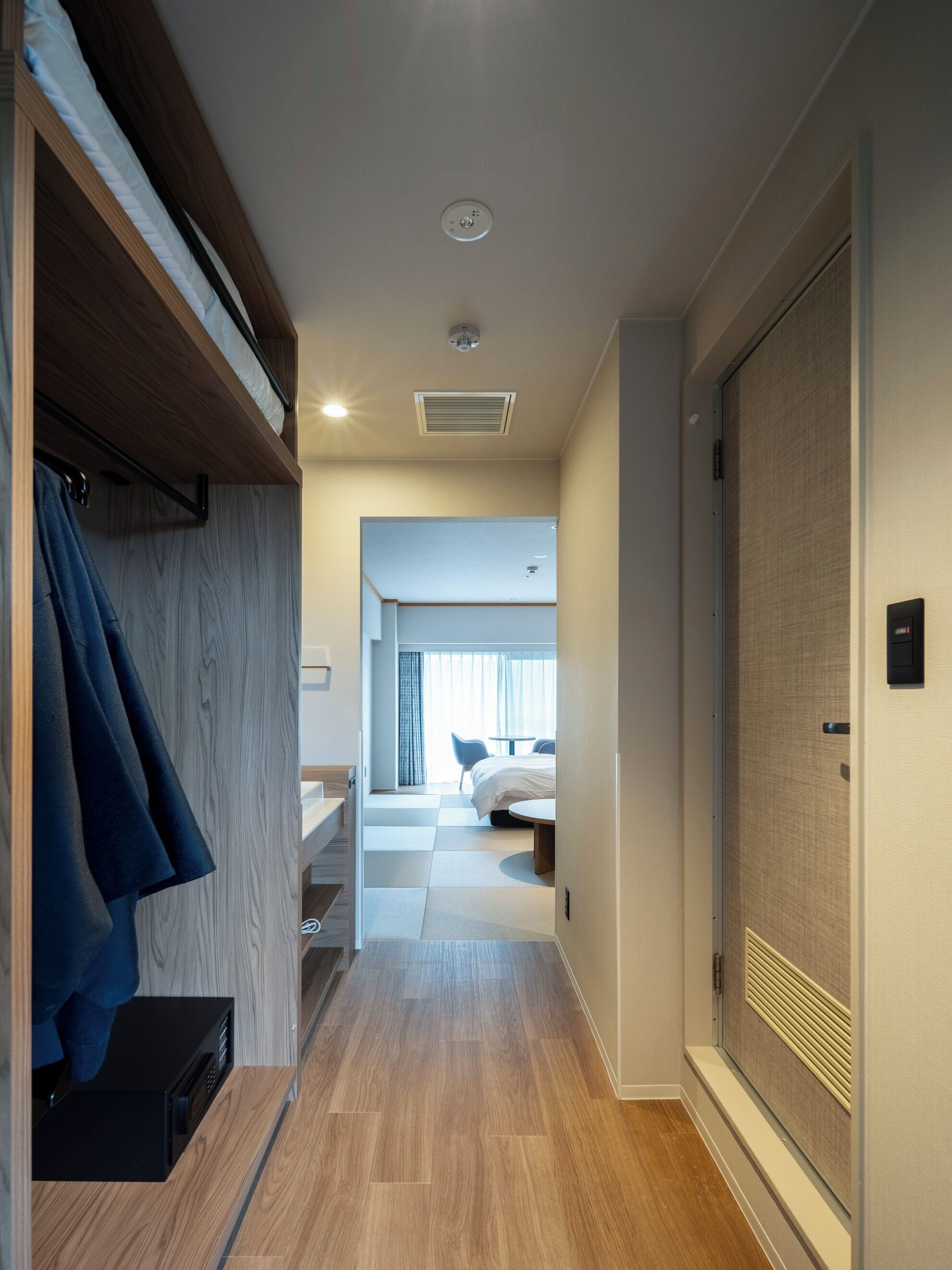 Corredor de hotel com armário de madeira, uma cama, uma escrivaninha e um banheiro.
