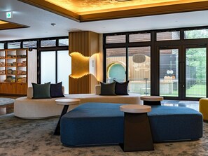 Un moderno vestíbulo de hotel con zona de estar, una estantería de madera y grandes ventanales.