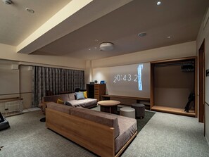 A modern living room with a sofa, coffee table, and a projection screen displaying the time. - B/C HOTEL KUSATSU (Kusatsu)