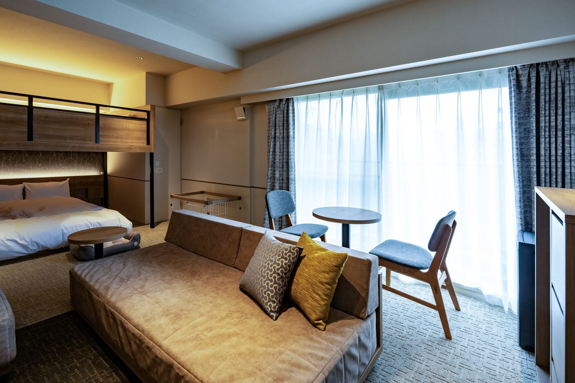 Een hotelkamer met een bed, een bank, een bijzettafeltje en een stoel. Er is een raam met gordijnen.