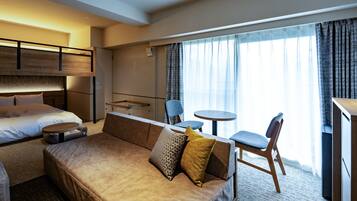Een hotelkamer met een bed, een bank, een bijzettafeltje en een stoel. Er is een raam met gordijnen.
