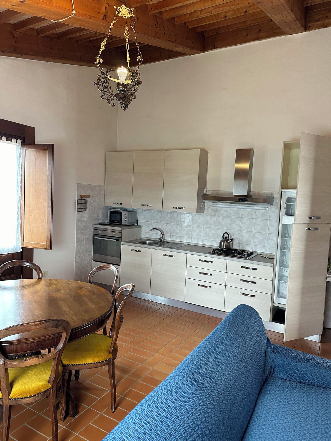 A compact kitchen with modern appliances, a dining area with a wooden table and chairs, and a blue sofa.