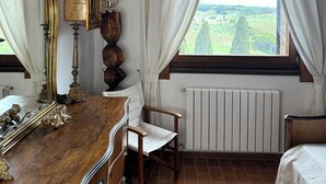 A bedroom with a wooden dresser, a chair, a bed, a window with curtains, and a radiator. - Podere Novo (Bibbona)