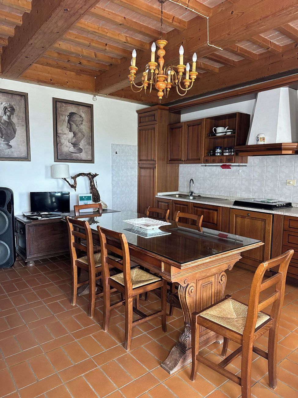 A dining area with a wooden table and chairs, a chandelier, and a kitchen with wooden cabinets and a tiled backsplash.