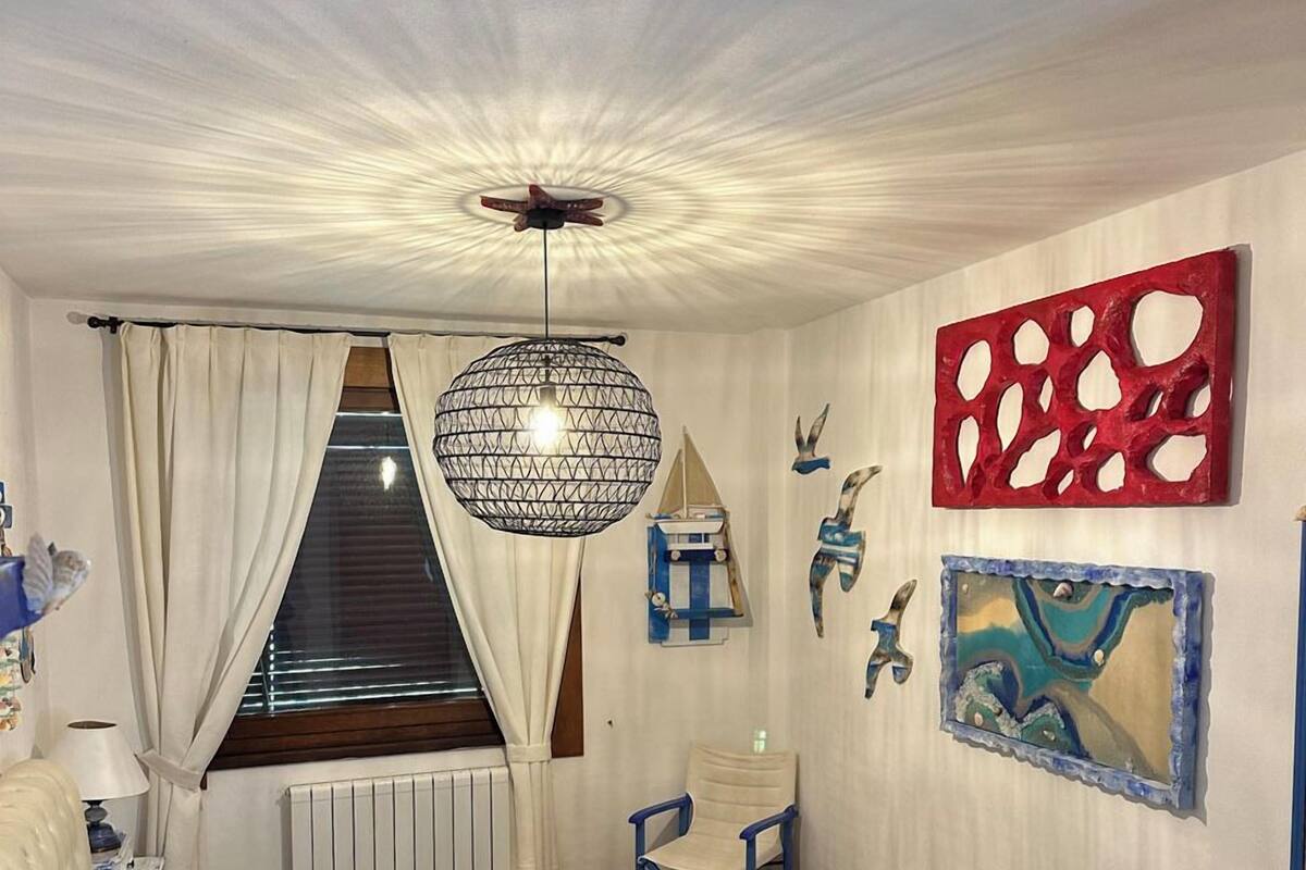 A bedroom with a bed, a desk, a chair, a hanging light fixture, and wall art.