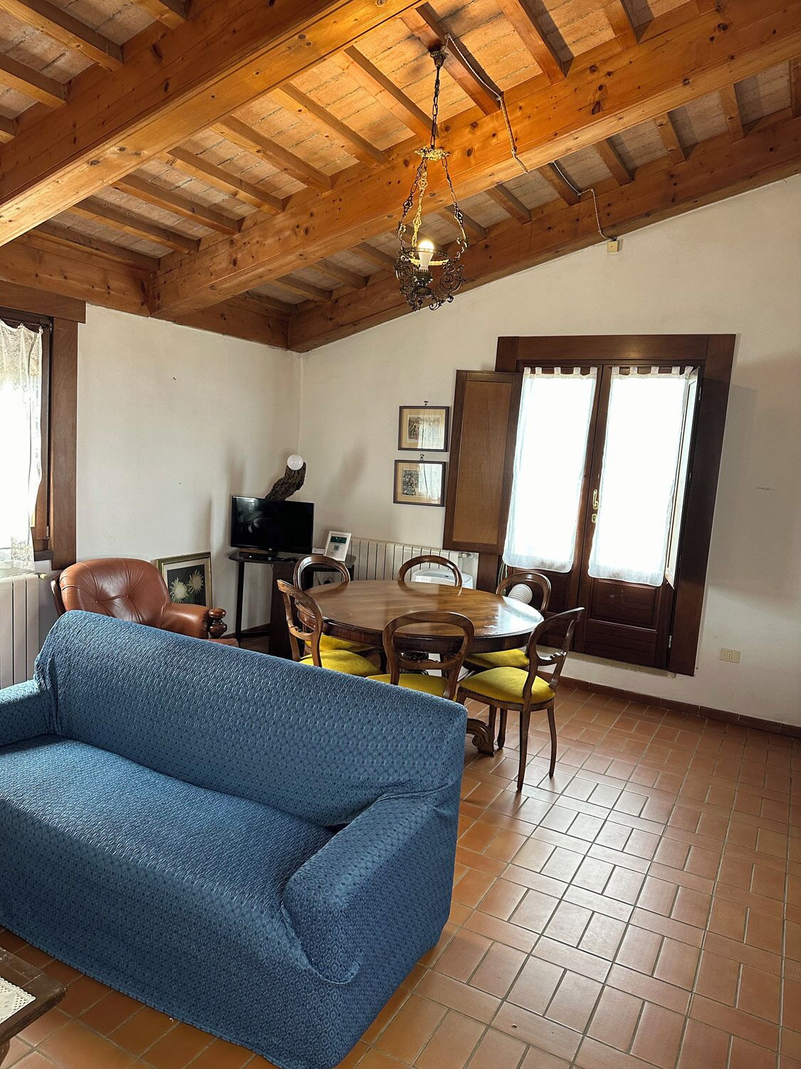 Ein Zimmer mit Holzboden, einem Esstisch mit Stühlen, einem Sofa und einem Fernseher.