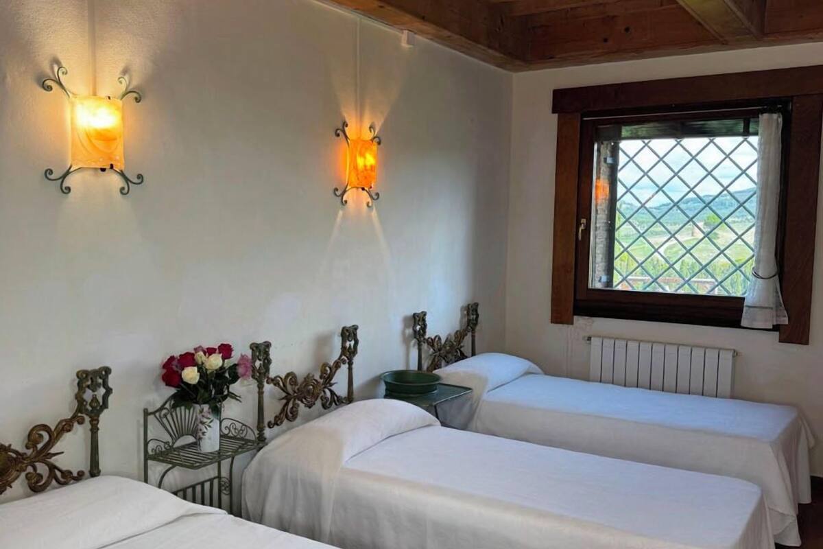A room with three beds, a window with a view, and wall-mounted lights.