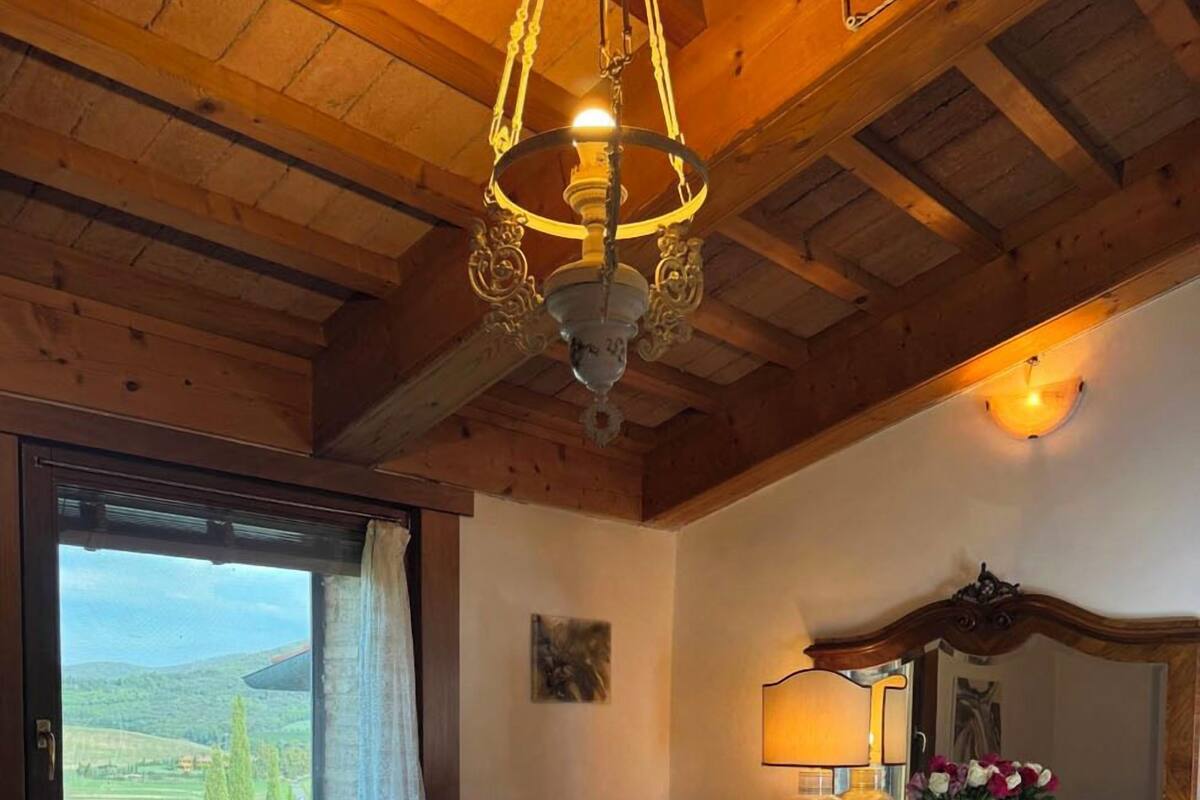 A room with a large window, wooden ceiling beams, a bed, a dresser, and a mirror.