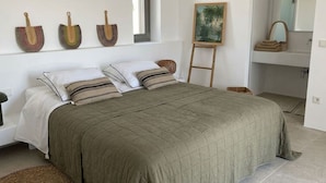 A bedroom with a large bed, a painting on the wall, and a bathroom with a mirror and towel rack. - Villa Lemoni – Walk to the Beach (4798+R23 Xifara, Greece)