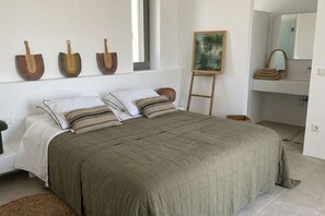 Ein Schlafzimmer mit einem großen Bett, einem Bild an der Wand und einem Badezimmer mit Spiegel und Handtuchhalter.
