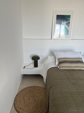 A bedroom with a bed, a bedside lamp, a picture on the wall, and a woven mat on the floor. - Villa Lemoni – Walk to the Beach (4798+R23 Xifara, Greece)