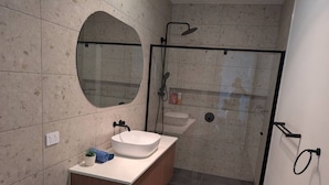 A modern bathroom with a round mirror, a sink, a shower, and a toilet.