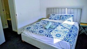 A single bed with a patterned bedspread and matching pillow, a white headboard, and a small bedside table.