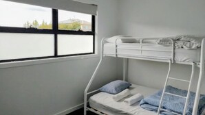 A bunk bed room with a window, white walls, and a view of trees and buildings.