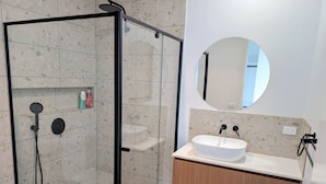 A modern bathroom with a glass-enclosed shower, a round mirror, and a wooden vanity with a white sink.