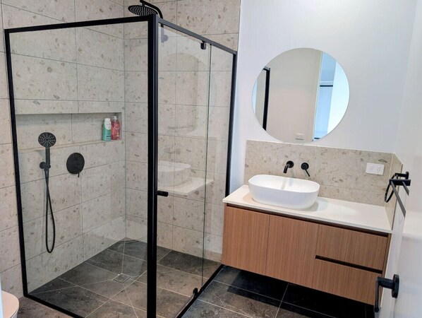 A modern bathroom with a glass-enclosed shower, a round mirror, and a wooden vanity with a white sink.
