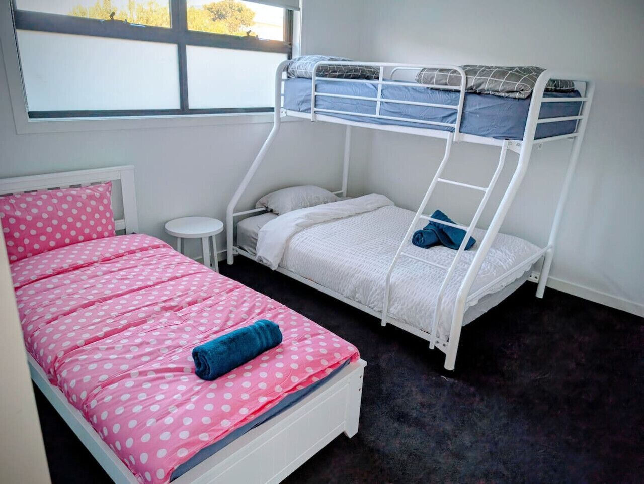 A bedroom with a bunk bed, a single bed, a small round table, and a window with a view.