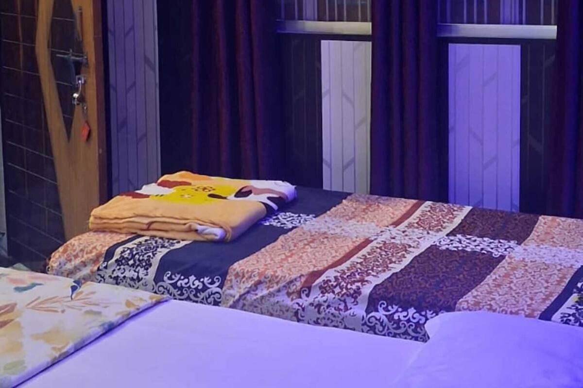 Una habitación de hotel con cama, ventana con cortinas, equipo de aire acondicionado y puerta de madera.