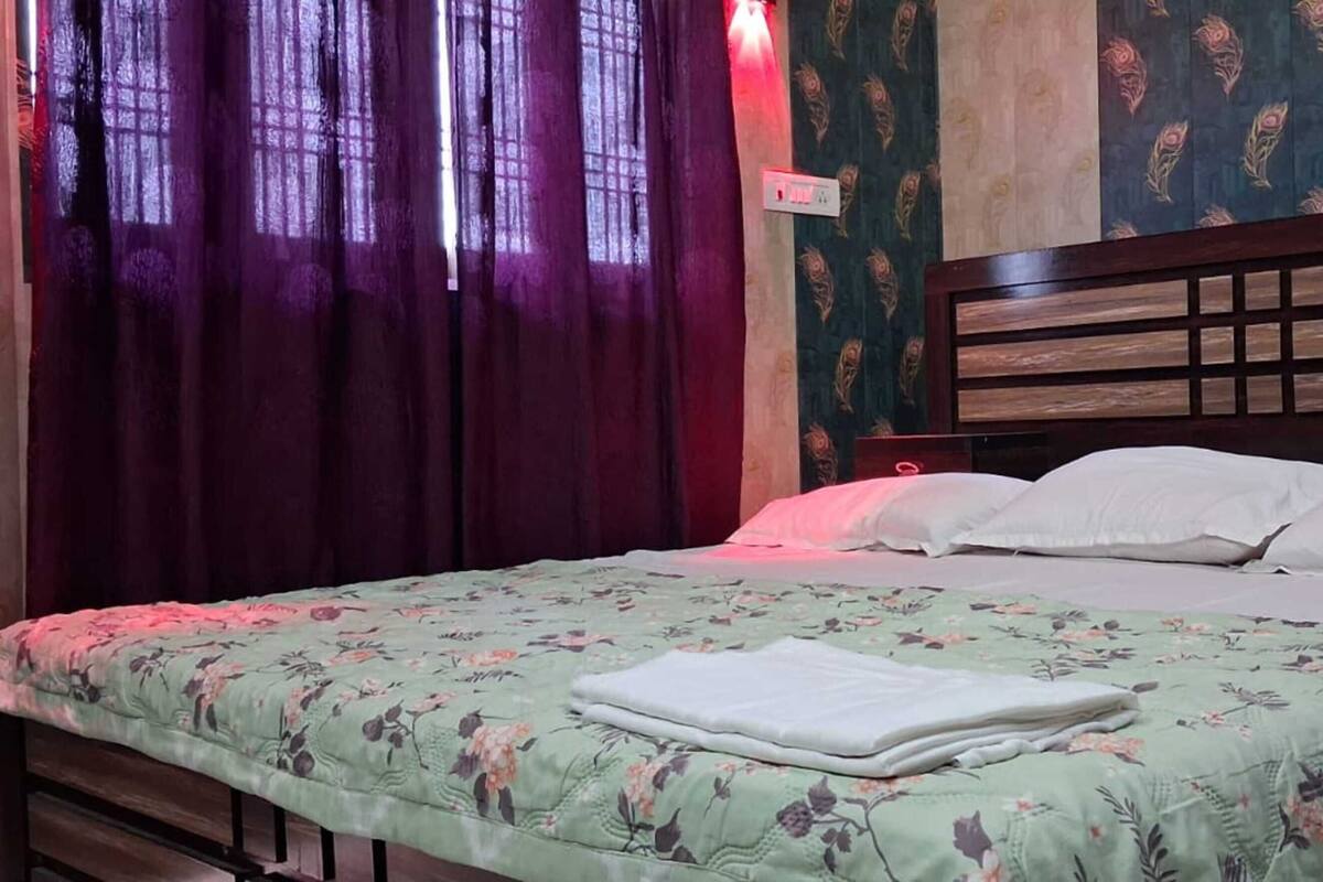 Una cama con una colcha estampada de flores, un cabecero de madera y una mesita de noche con una lámpara.